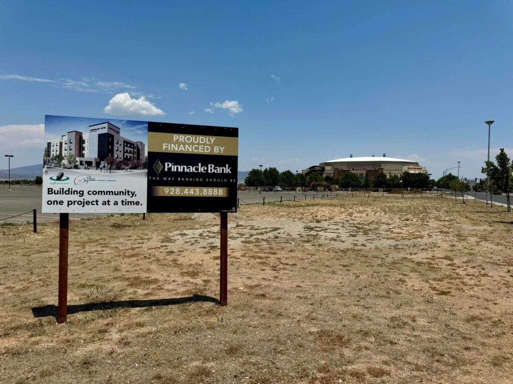 Photo shows a sign presenting the new construction project with a wide open space for the project in the background.