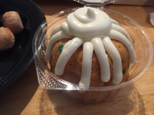 Nothing Bundt Cake with icing in a plastic serving container on a wood surface.